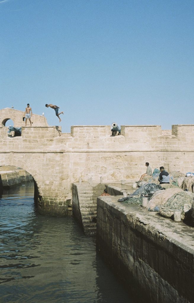 Fotografia de nois banyant-se al port d'Essouira, Marroc, capturada per Júlia Olivé Studio, artista multidisciplinar especialitzada en fotografia, disseny i il·lustració.
